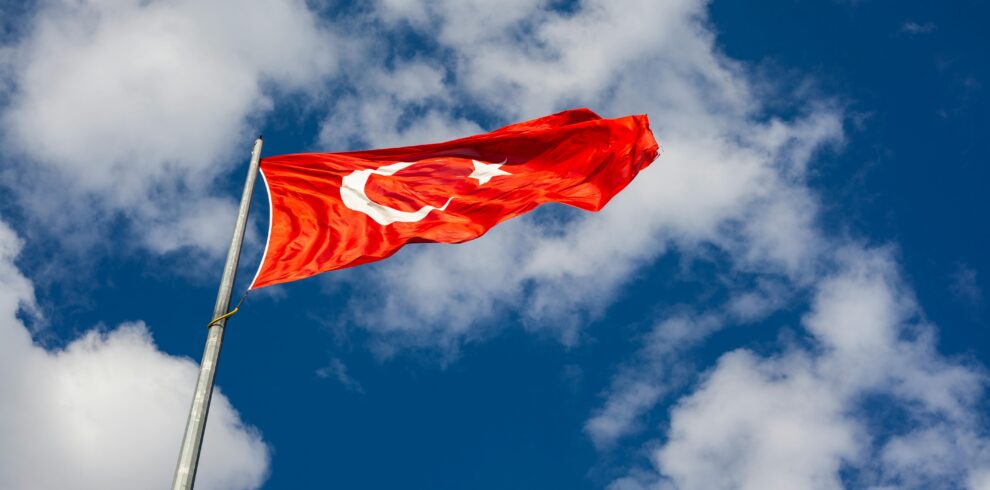 Low angle view of Turkish flag waving against a bright sky, symbolizing national pride and freedom.