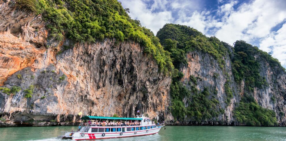 A boat cruise offers breathtaking views of lush cliffs under a bright blue sky.