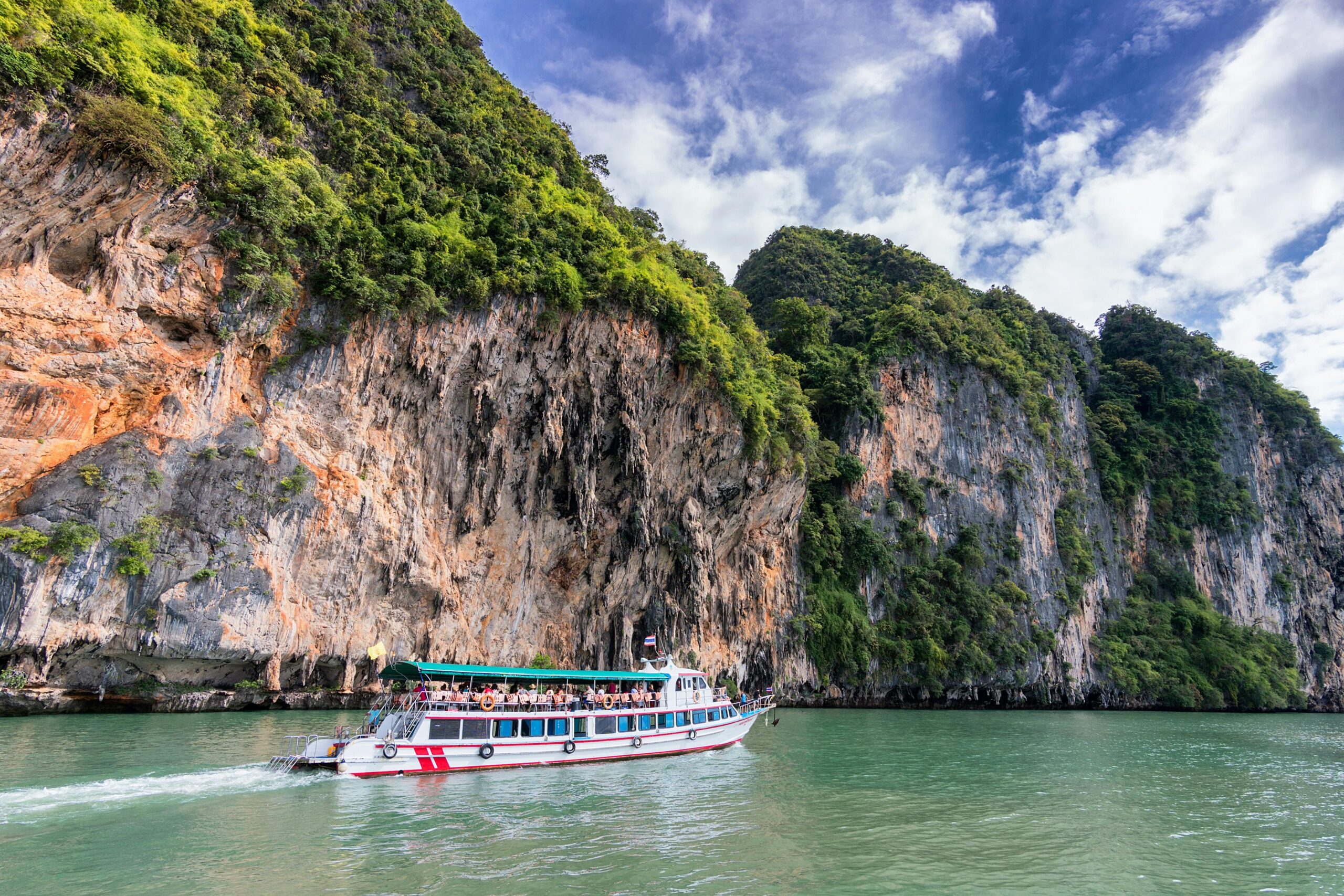 A boat cruise offers breathtaking views of lush cliffs under a bright blue sky.